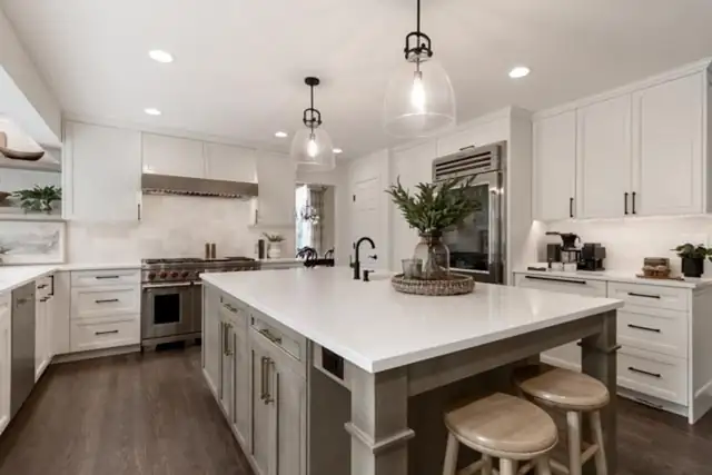 White kitchen remodel with shaker cabinets, a gray island with white quartz top, glass pendants and wood counter stools