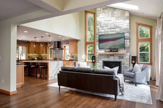 Squak Mountain Retreat great room in Issaquah with a full-height stone fireplace, wood-trimmed windows and the open kitchen beyond
