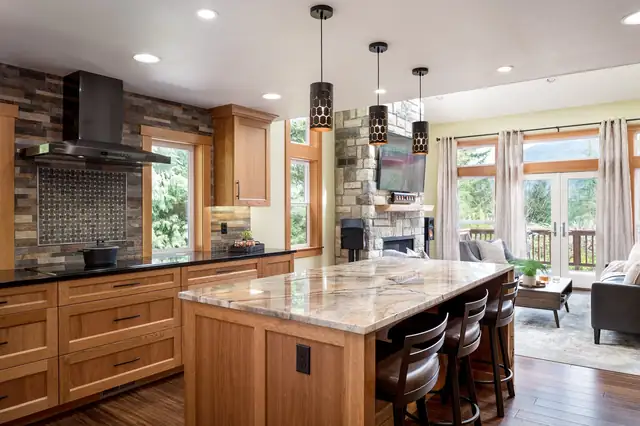 Squak Mountain Retreat kitchen remodel in Issaquah with wood shaker cabinets, a quartzite island, black range hood and stone fireplace beyond