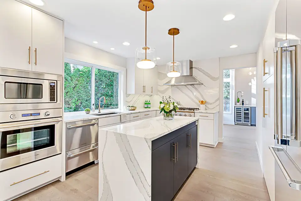 Kitchen remodeling Issaquah: Modern Moment kitchen with a quartz waterfall island, full-height slab backsplash, white cabinets and brass pendants