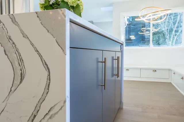 Close-up of a waterfall quartz edge on a blue-gray island with brushed brass pulls