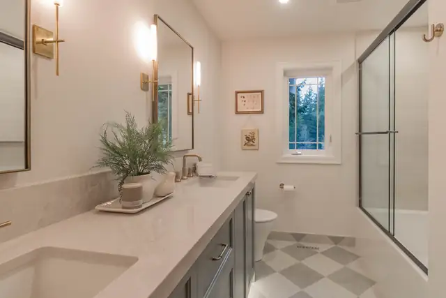 Elegant and Timeless bathroom remodel in North Bend with a long quartz vanity, brass sconces, checkerboard tile floor and glass shower